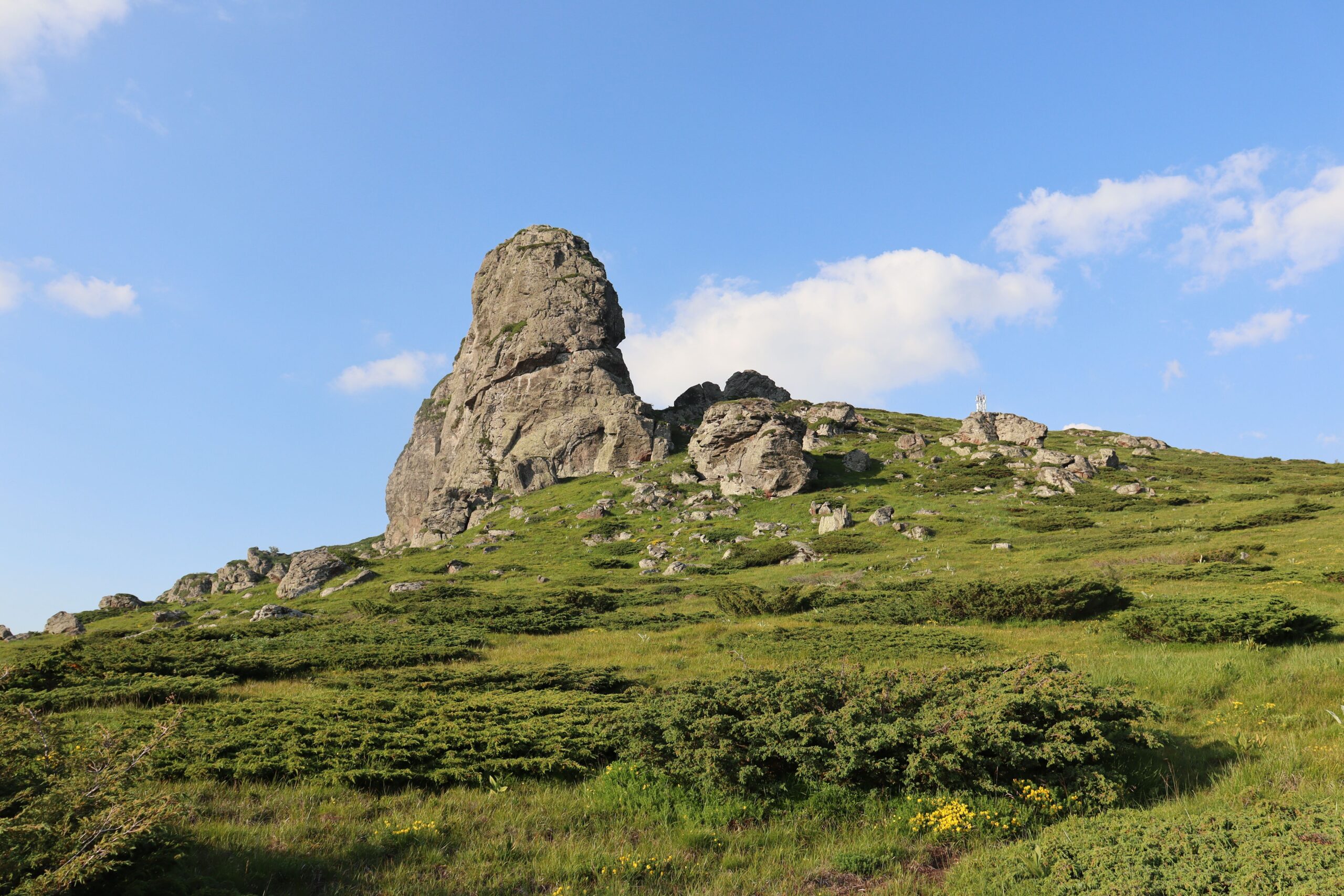 A stunning rocky hill under clear skies, surrounded by lush greenery.